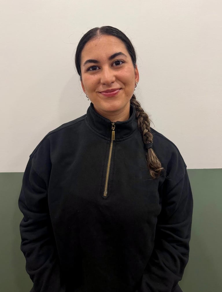 Woman with dark braided hair wearing a black quarter-zip pullover, smiling at the camera against a neutral background